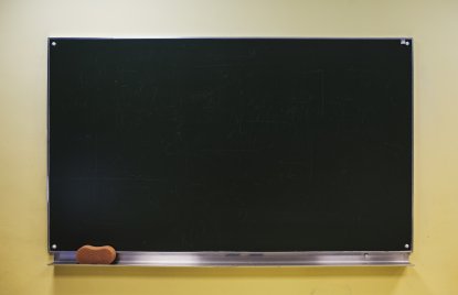 Eine unbeschriebene, schwarze Tafel, in deren Ablage sich links ein brauner Tafelschwamm befindet