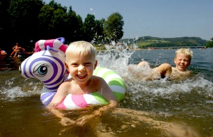2 Kinder baden in einem See und lachen in die Kamera
