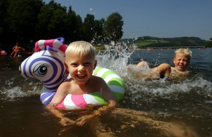 Das Foto zeigt 2 Kinder, die im See baden und sich freuen.