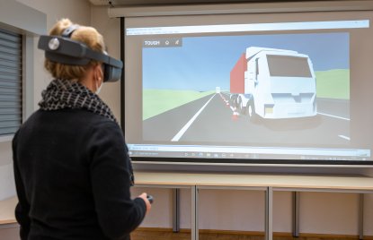eine VR-Brille tragende Frau steuert einen digitalen LKW vor einer Leinwand