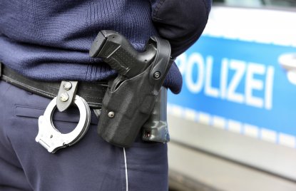 Polizist mit Waffe vor Polizeiwagen