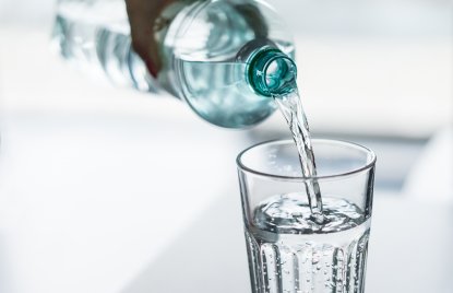 Eine Hand gießt aus einer Flasche Wasser in ein Glas.