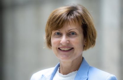 Eine Frau mit kurzen, hellbraunen Haaren und blauem Blazer lächelt 