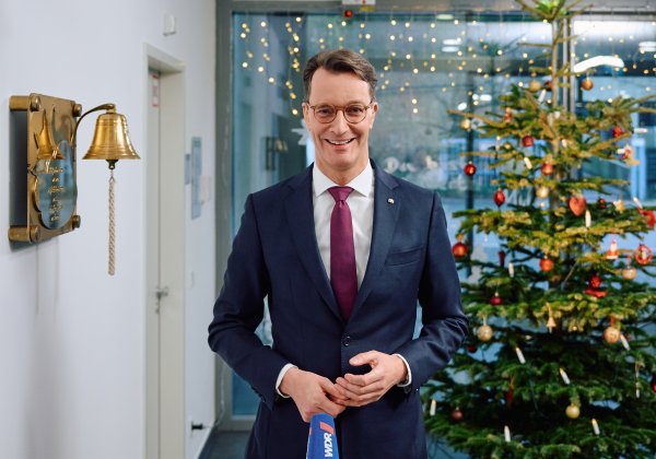 Ministerpräsident Hendrik Wüst steht auf einem Flur in einem Krankenhaus vor einem Weihnachtsbaum 